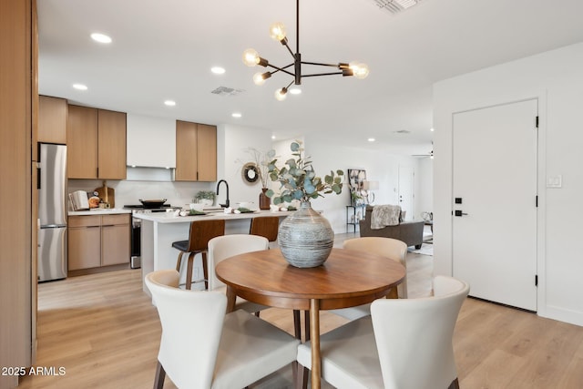 dining space with sink, a chandelier, and light hardwood / wood-style floors