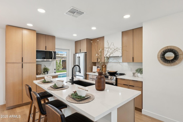 kitchen with a kitchen island with sink, sink, light wood-type flooring, and appliances with stainless steel finishes