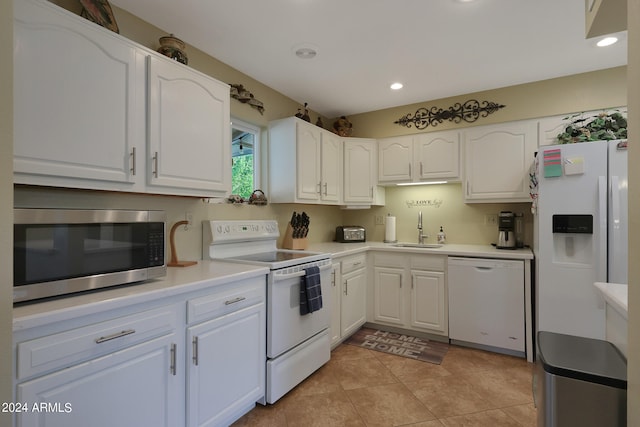 kitchen with light tile patterned flooring, white appliances, sink, and white cabinetry