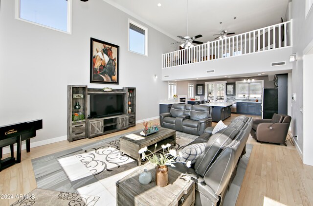 living room with a towering ceiling, light wood-type flooring, and ceiling fan