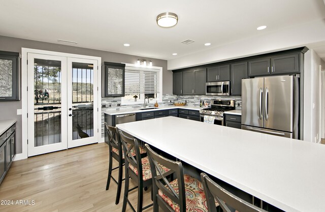 kitchen featuring backsplash, stainless steel appliances, light hardwood / wood-style flooring, french doors, and sink