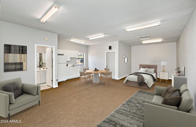 bedroom with sink, carpet, white fridge, and ensuite bath