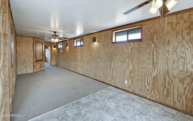 basement with ceiling fan, light carpet, and wooden walls