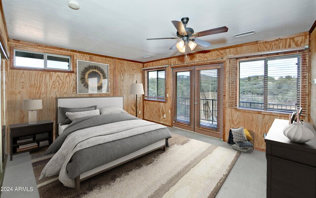 carpeted bedroom with wood walls, ceiling fan, and access to outside