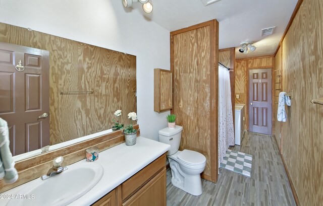 bathroom with wooden walls, washer / clothes dryer, vanity, and toilet