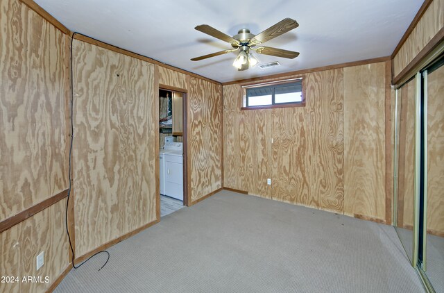 spare room with ceiling fan, washer / dryer, light colored carpet, and wooden walls