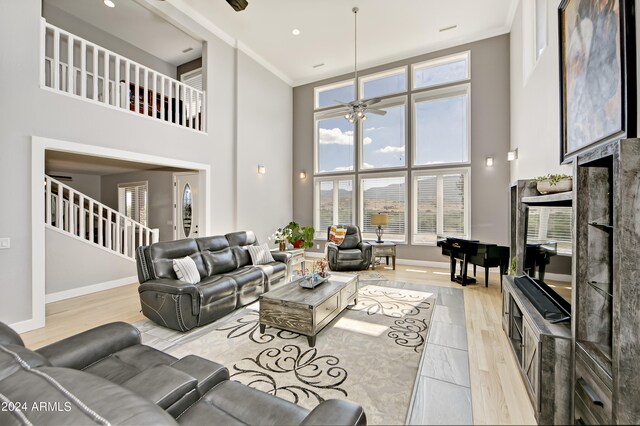 living room featuring ceiling fan, light hardwood / wood-style flooring, a high ceiling, and ornamental molding