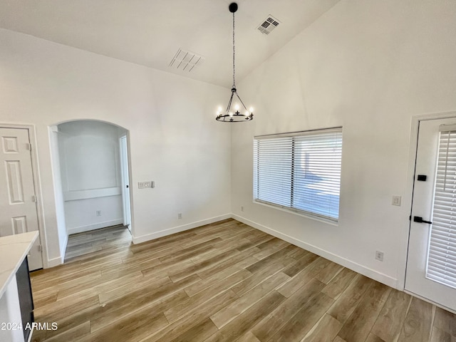 unfurnished dining area with a chandelier, light wood-type flooring, and high vaulted ceiling