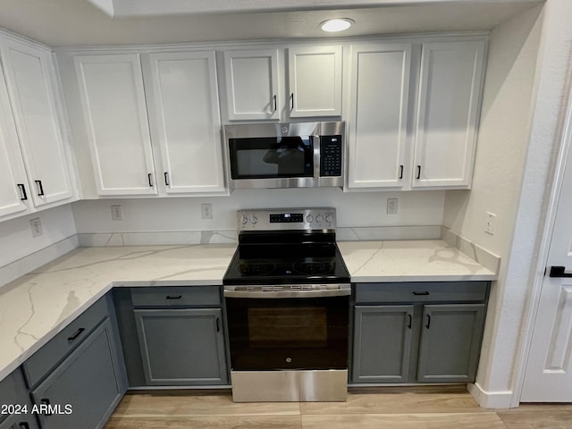 kitchen featuring light wood-type flooring, light stone counters, gray cabinetry, stainless steel appliances, and white cabinets