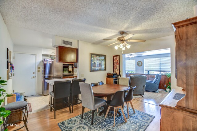 dining space with a textured ceiling, light wood-type flooring, and visible vents