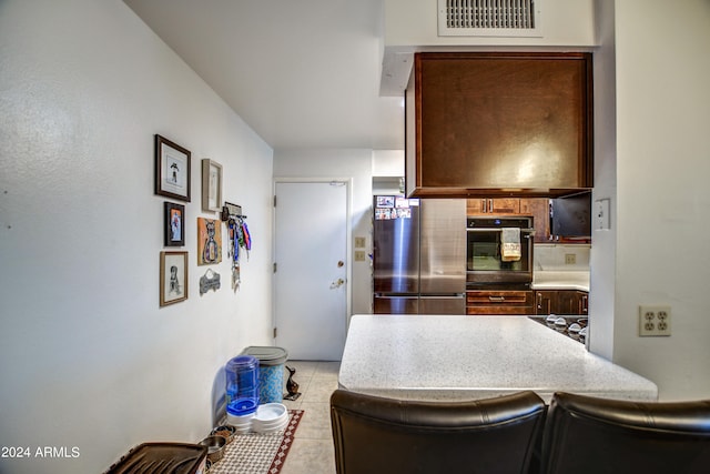 kitchen featuring light tile patterned flooring, stainless steel refrigerator, and black oven