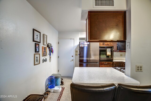 kitchen with light countertops, visible vents, freestanding refrigerator, light tile patterned flooring, and oven