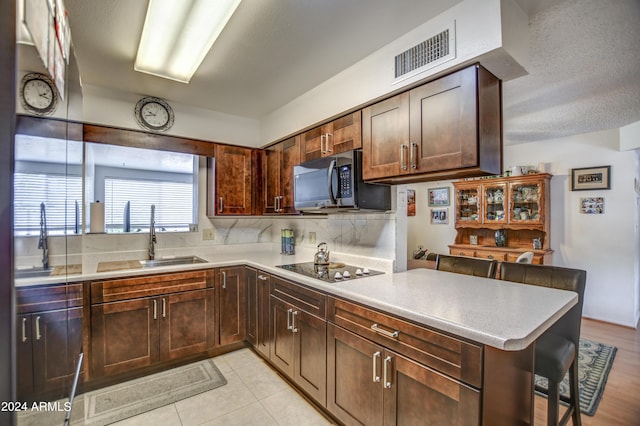 kitchen featuring light hardwood / wood-style flooring, backsplash, kitchen peninsula, sink, and black electric cooktop