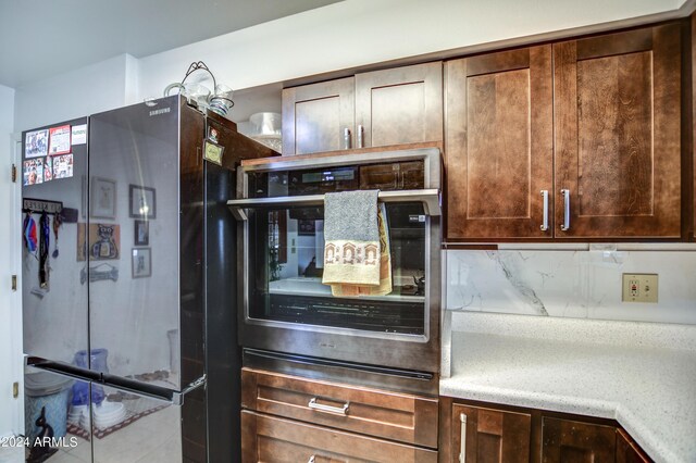 kitchen with wall oven, dark brown cabinets, backsplash, and freestanding refrigerator