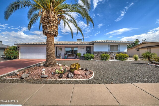 ranch-style home with concrete driveway, covered porch, a garage, stone siding, and a tiled roof