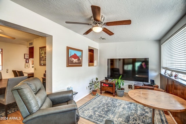 living room with a textured ceiling, ceiling fan, and hardwood / wood-style floors