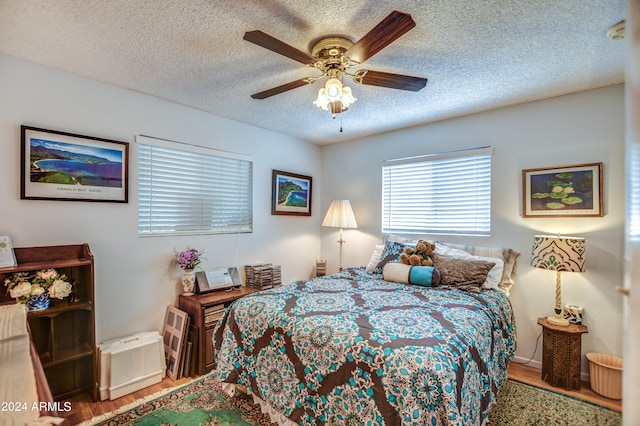 bedroom with hardwood / wood-style floors, ceiling fan, and a textured ceiling