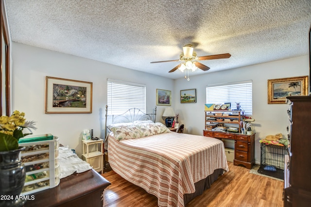 bedroom featuring a textured ceiling, ceiling fan, hardwood / wood-style floors, and multiple windows