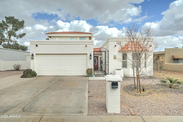 mediterranean / spanish-style home featuring a tile roof, concrete driveway, stucco siding, an attached garage, and a gate