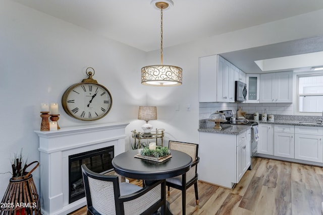 kitchen with a sink, light stone counters, a glass covered fireplace, stainless steel appliances, and light wood-style floors