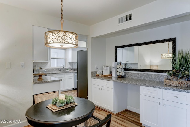 kitchen featuring visible vents, a sink, light wood-style floors, white cabinetry, and decorative light fixtures