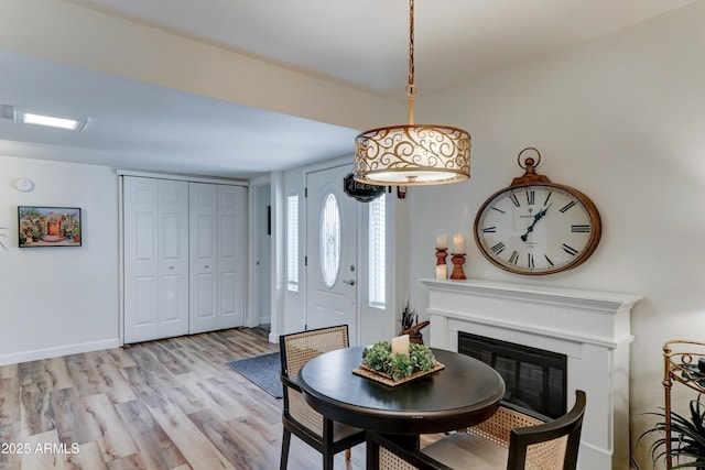 dining area with a glass covered fireplace, light wood-style flooring, and baseboards