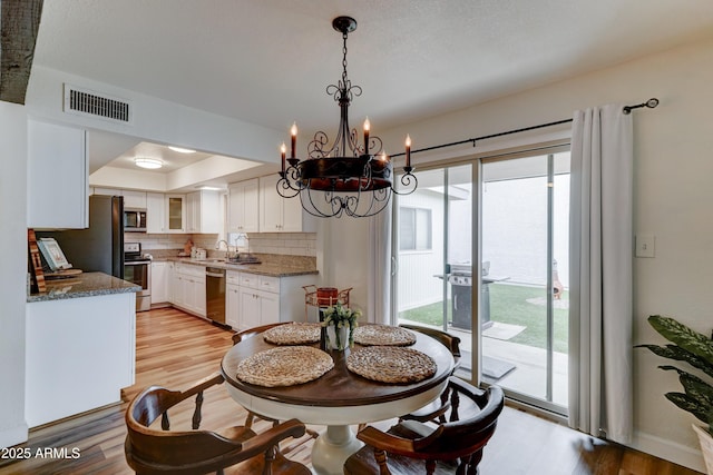 dining area with visible vents, a raised ceiling, a chandelier, and light wood finished floors