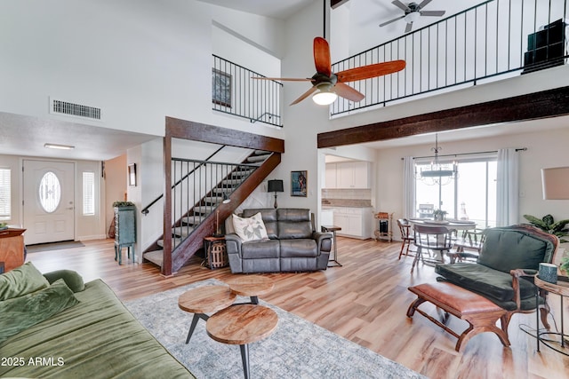 living room with visible vents, stairs, light wood-style floors, ceiling fan with notable chandelier, and a wealth of natural light