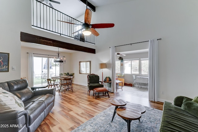 living area with beamed ceiling, ceiling fan with notable chandelier, light wood-type flooring, and a wealth of natural light