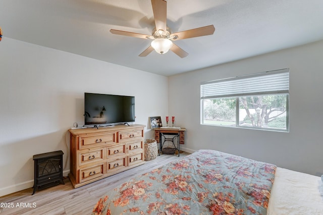 bedroom featuring baseboards, a ceiling fan, wood finished floors, and a wood stove