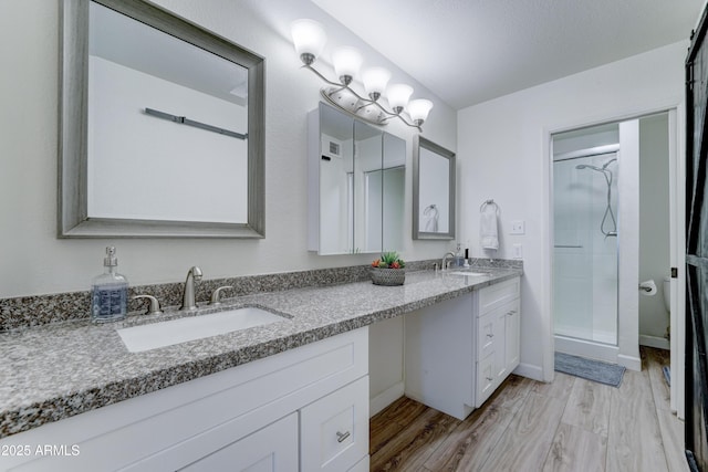 bathroom featuring a sink, a shower stall, wood finished floors, and double vanity