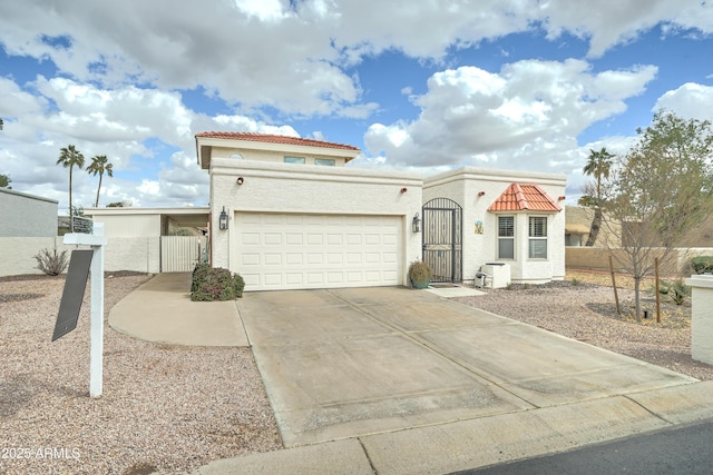 mediterranean / spanish-style house featuring stucco siding, a tile roof, a gate, fence, and concrete driveway