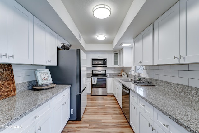 kitchen featuring a sink, stainless steel appliances, white cabinets, a raised ceiling, and light wood-type flooring