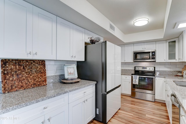 kitchen with visible vents, backsplash, a tray ceiling, light wood-style flooring, and appliances with stainless steel finishes