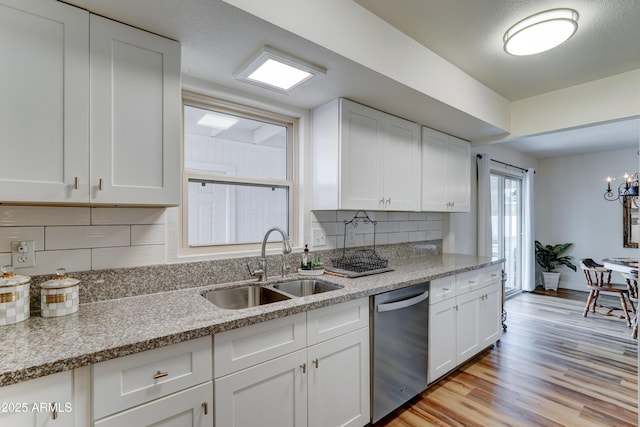 kitchen with light wood-type flooring, a sink, tasteful backsplash, stainless steel dishwasher, and white cabinets