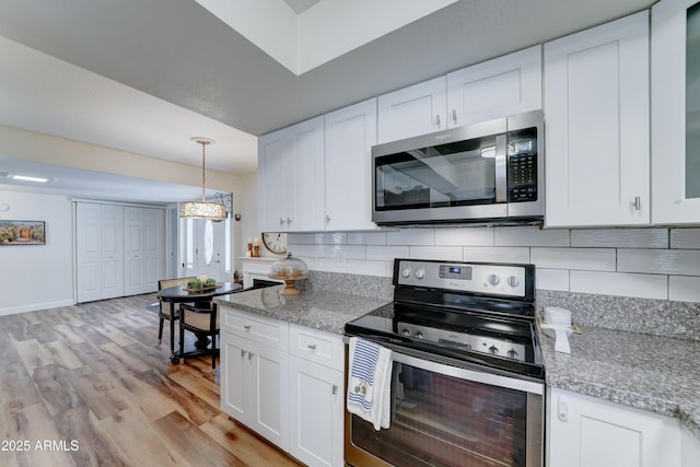 kitchen featuring light wood finished floors, stainless steel appliances, hanging light fixtures, white cabinets, and backsplash