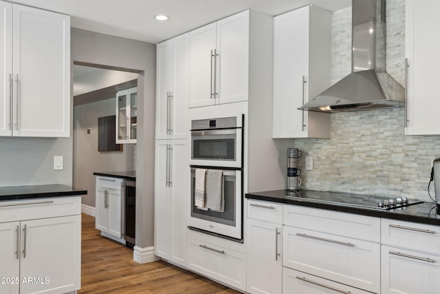 kitchen featuring wall chimney range hood, dark countertops, black electric cooktop, double oven, and wine cooler