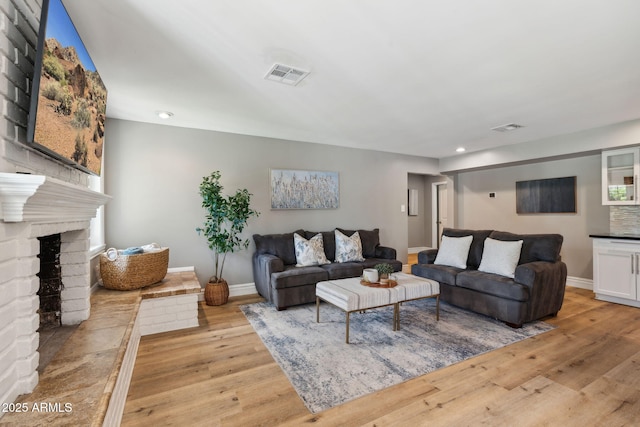 living room with a brick fireplace, recessed lighting, visible vents, and light wood finished floors