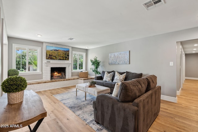 living room featuring baseboards, visible vents, light wood-style flooring, and a fireplace