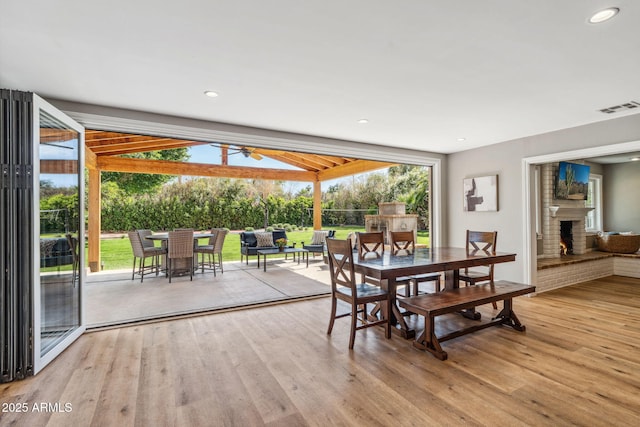 dining space featuring a ceiling fan, visible vents, a fireplace, wood finished floors, and a wealth of natural light