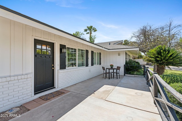 entrance to property with board and batten siding, brick siding, a shingled roof, and outdoor dining area