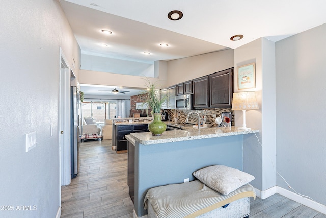 8510 W Joan De Arc Ave, Peoria, AZ 85381 - kitchen featuring decorative backsplash, dark brown cabinetry, stainless steel appliances, light wood-style flooring, and a peninsula