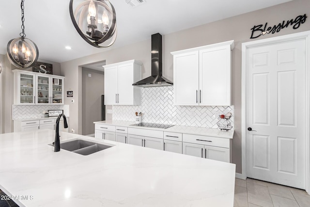 kitchen featuring black electric stovetop, light stone countertops, wall chimney range hood, sink, and white cabinetry