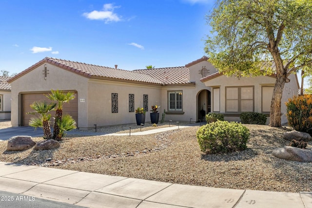 mediterranean / spanish home featuring stucco siding, driveway, a tile roof, and a garage