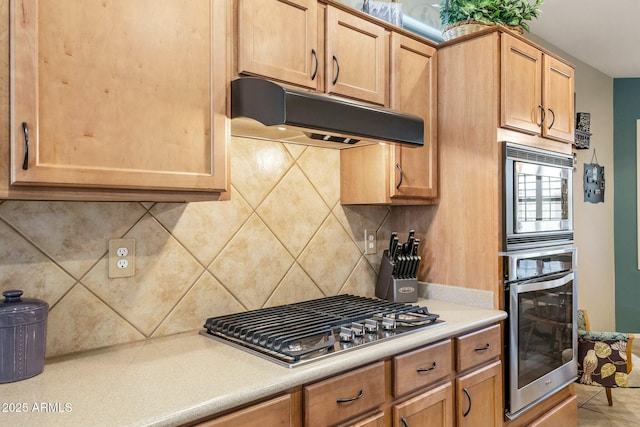 kitchen with under cabinet range hood, stainless steel appliances, tasteful backsplash, and light countertops