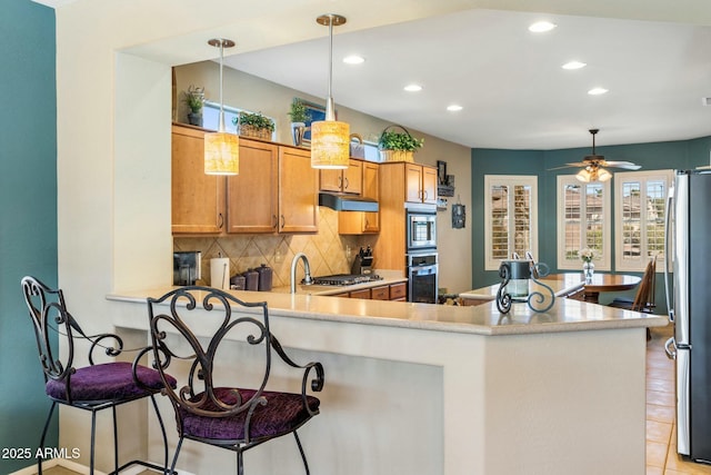 kitchen featuring tasteful backsplash, under cabinet range hood, light countertops, recessed lighting, and stainless steel appliances