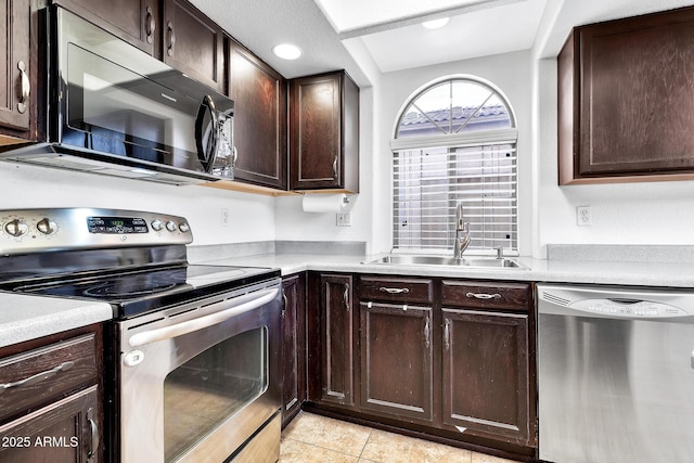 kitchen with appliances with stainless steel finishes, sink, dark brown cabinets, and light tile patterned floors