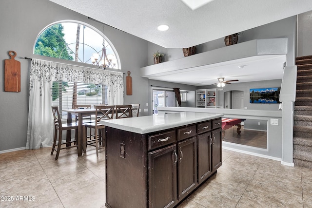 kitchen with light tile patterned floors, dark brown cabinets, a center island, and ceiling fan