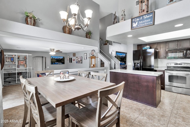 dining space with a high ceiling, ceiling fan with notable chandelier, and light tile patterned floors