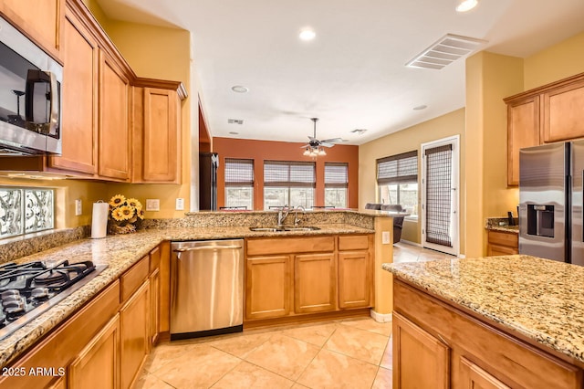 kitchen with visible vents, a peninsula, brown cabinetry, stainless steel appliances, and a sink